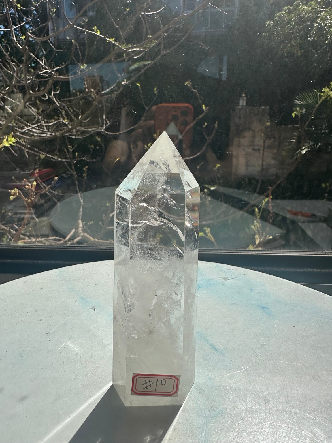 Brazilian clear quartz tower number 10, 280g and 14cm tall: full view with identifying label and a long shadow in natural sunlight.