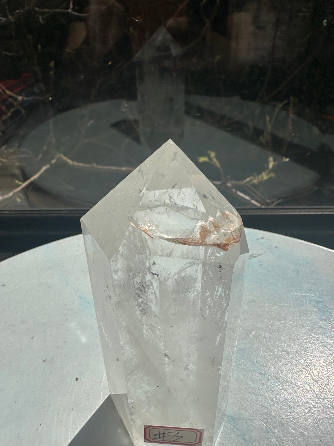 Close-up of the pointed top of clear quartz tower number 3, showing the curved brown inclusion and intersecting internal fracture lines beneath polished facets.