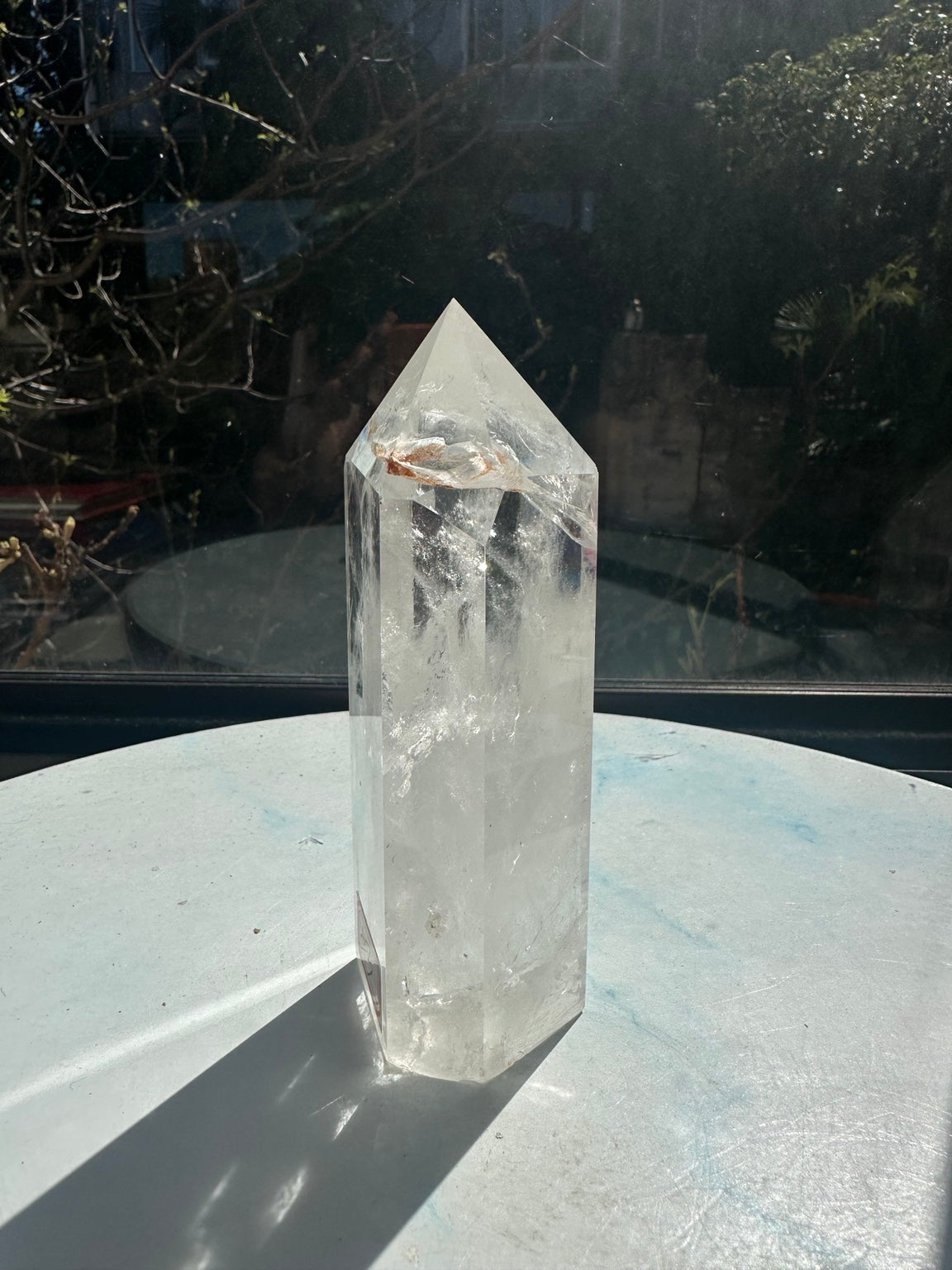 Narrow side view of the 467g clear quartz tower, showing polished facets, the flat base, internal veils and a brown inclusion below the pointed top.