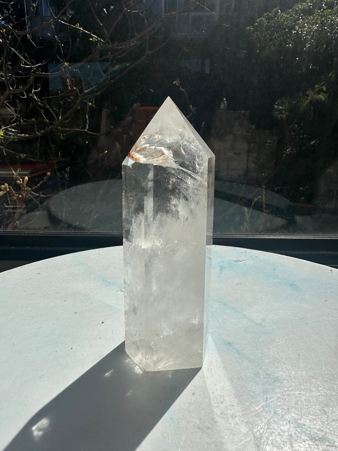 Alternative side of Brazilian clear quartz point number 3, showing clear upper areas and cloudy white textures through the lower body while standing upright in sunlight.