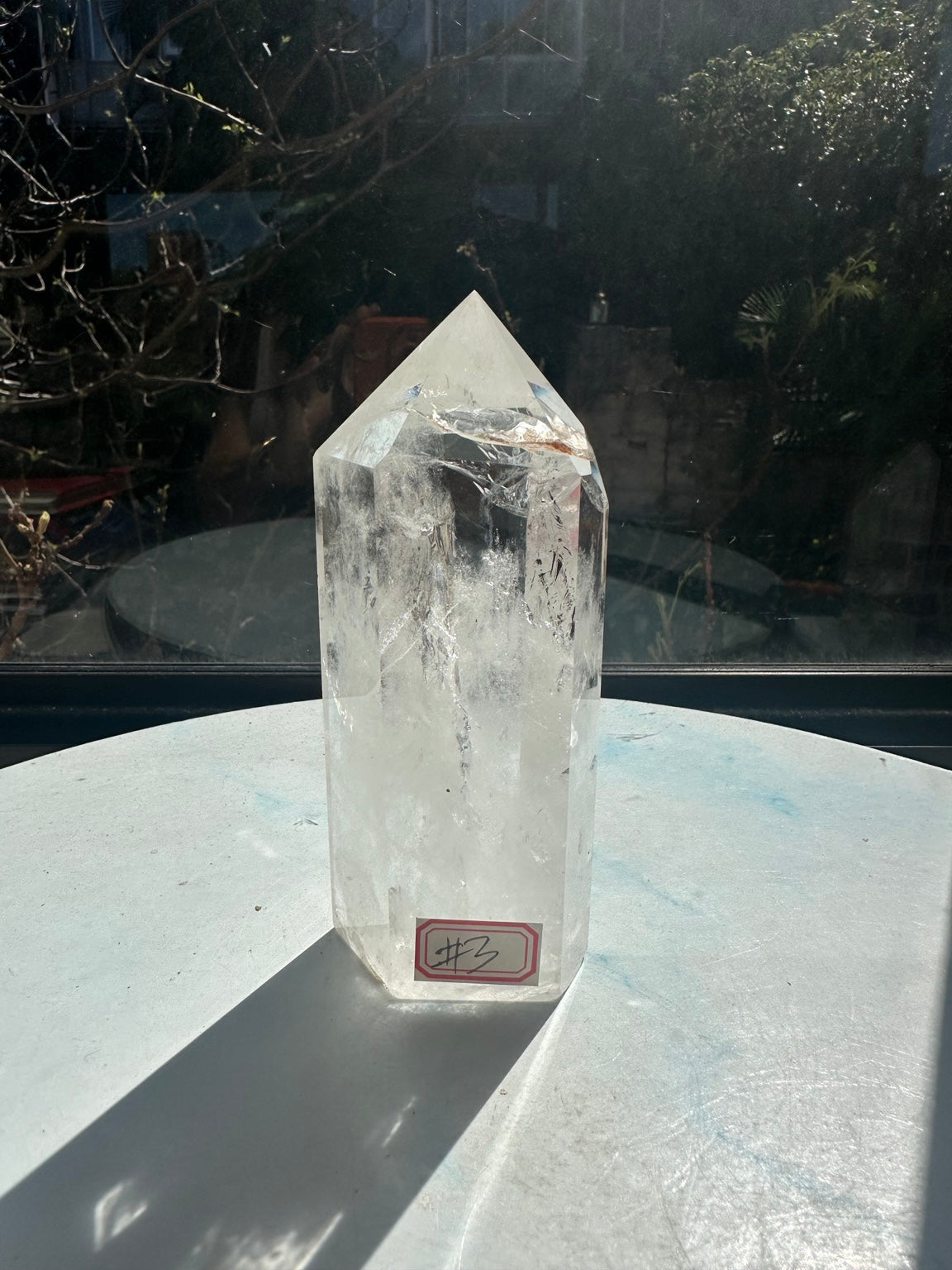 Labelled front angle of the exact clear quartz tower number 3, showing its pointed top, transparent facets, dark flecks and milky white lower section.