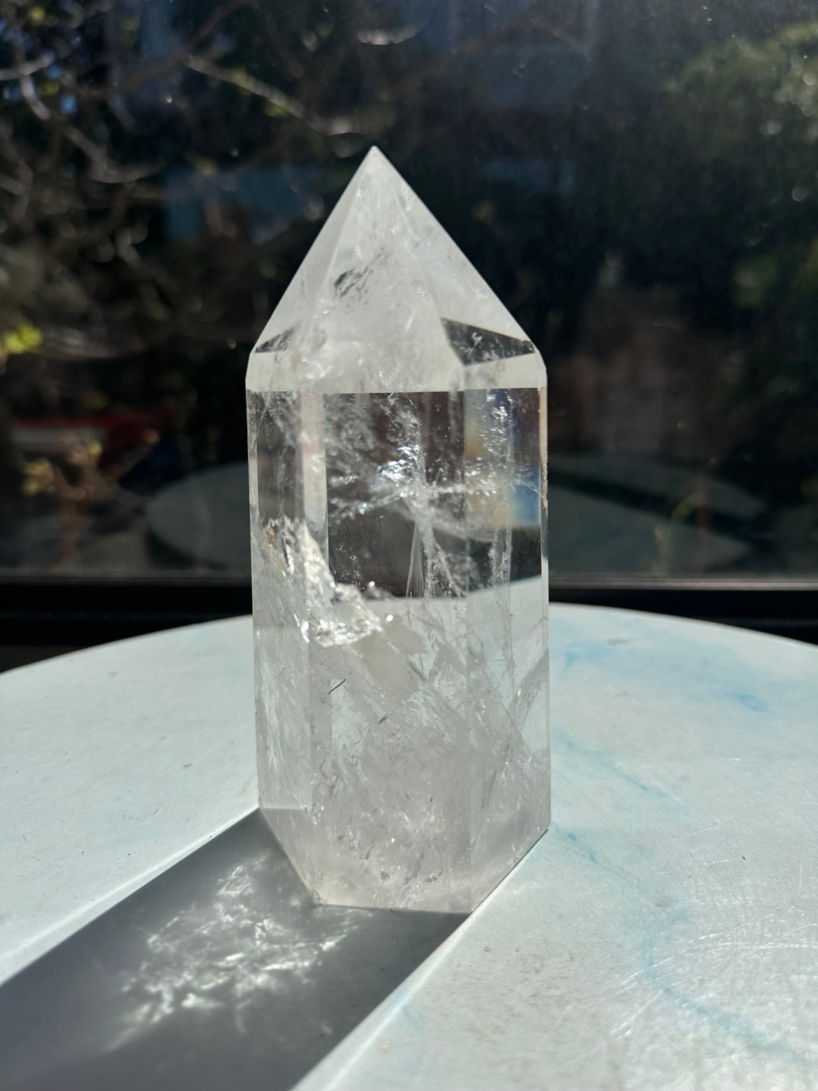 Brazilian clear quartz tower number 7, 789g and 14cm tall, showing its polished point, transparent upper section and white internal veils in sunlight.