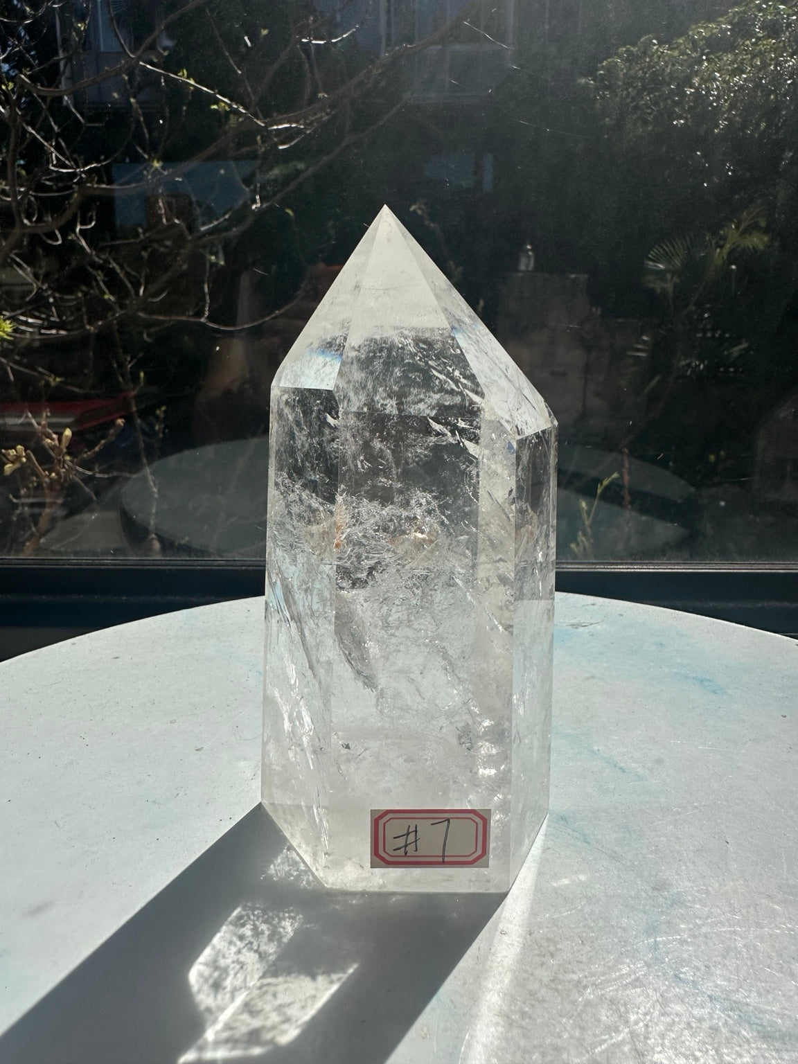 Front view of the exact 789g clear quartz tower with number 7 label, polished pointed top and cloudy white inclusions near the base.