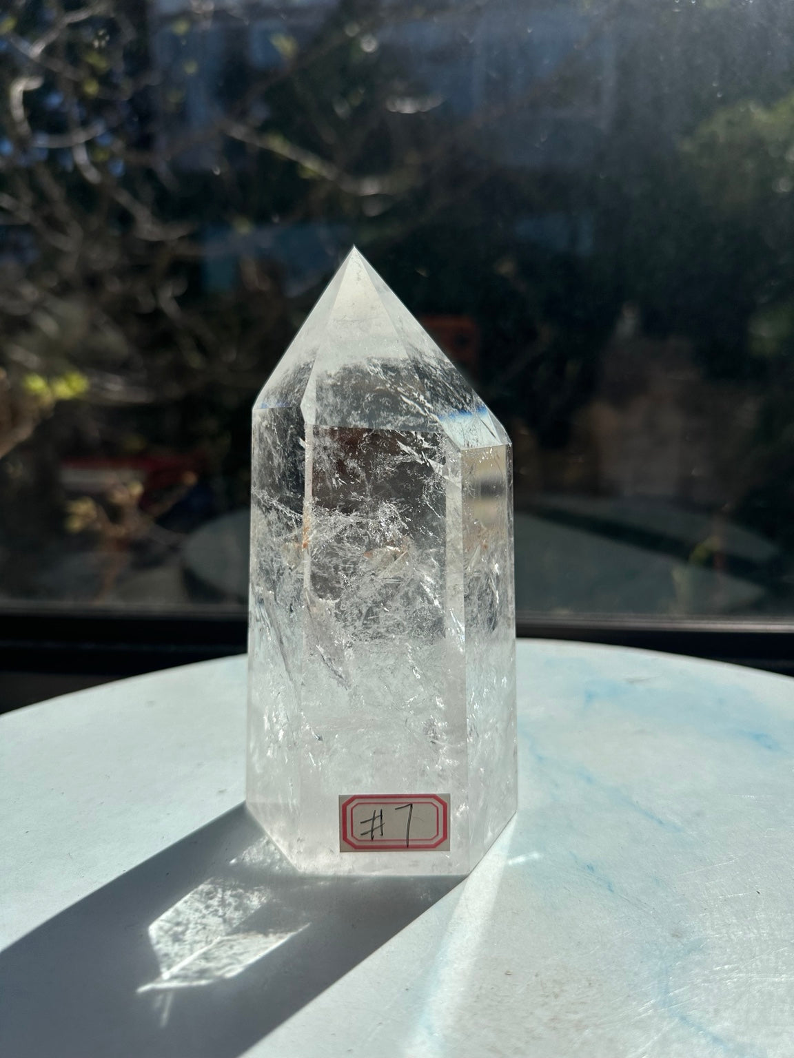 Full front view of the exact clear quartz tower with number 7 label, faceted point and natural internal veils.