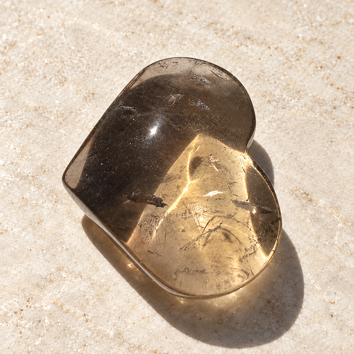 Brazilian smoky quartz heart on a neutral stone surface, showing polished tea-brown translucency and natural inclusions