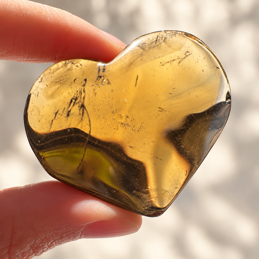 Smoky quartz heart held in natural light to show translucency and internal mineral details