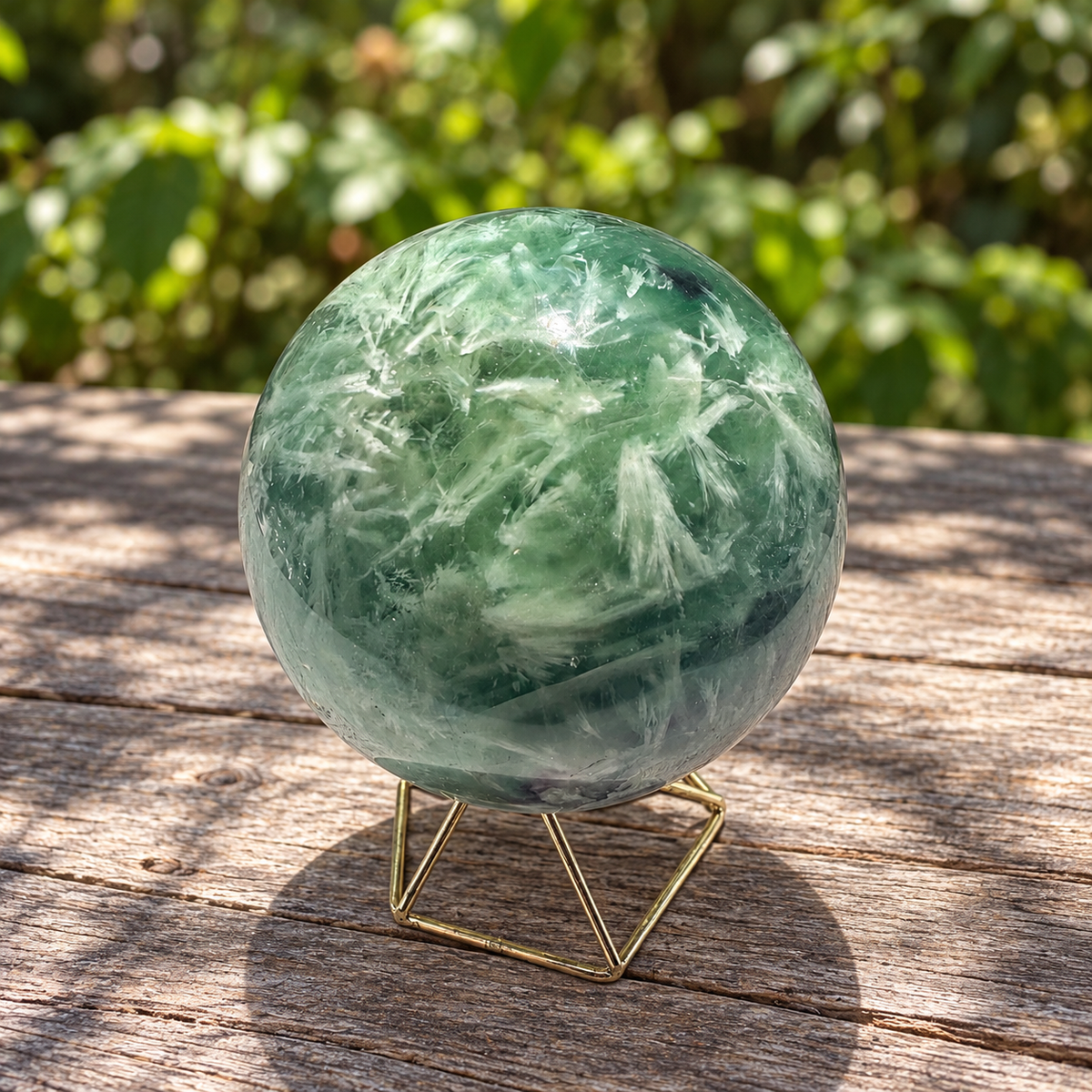 White feather-like formations across the green side of exact fluorite sphere No.4 on a weathered wooden table