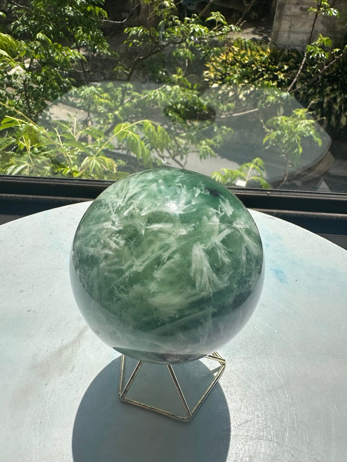 Unedited original photograph of exact feather fluorite sphere No.1 on its stand in natural window light