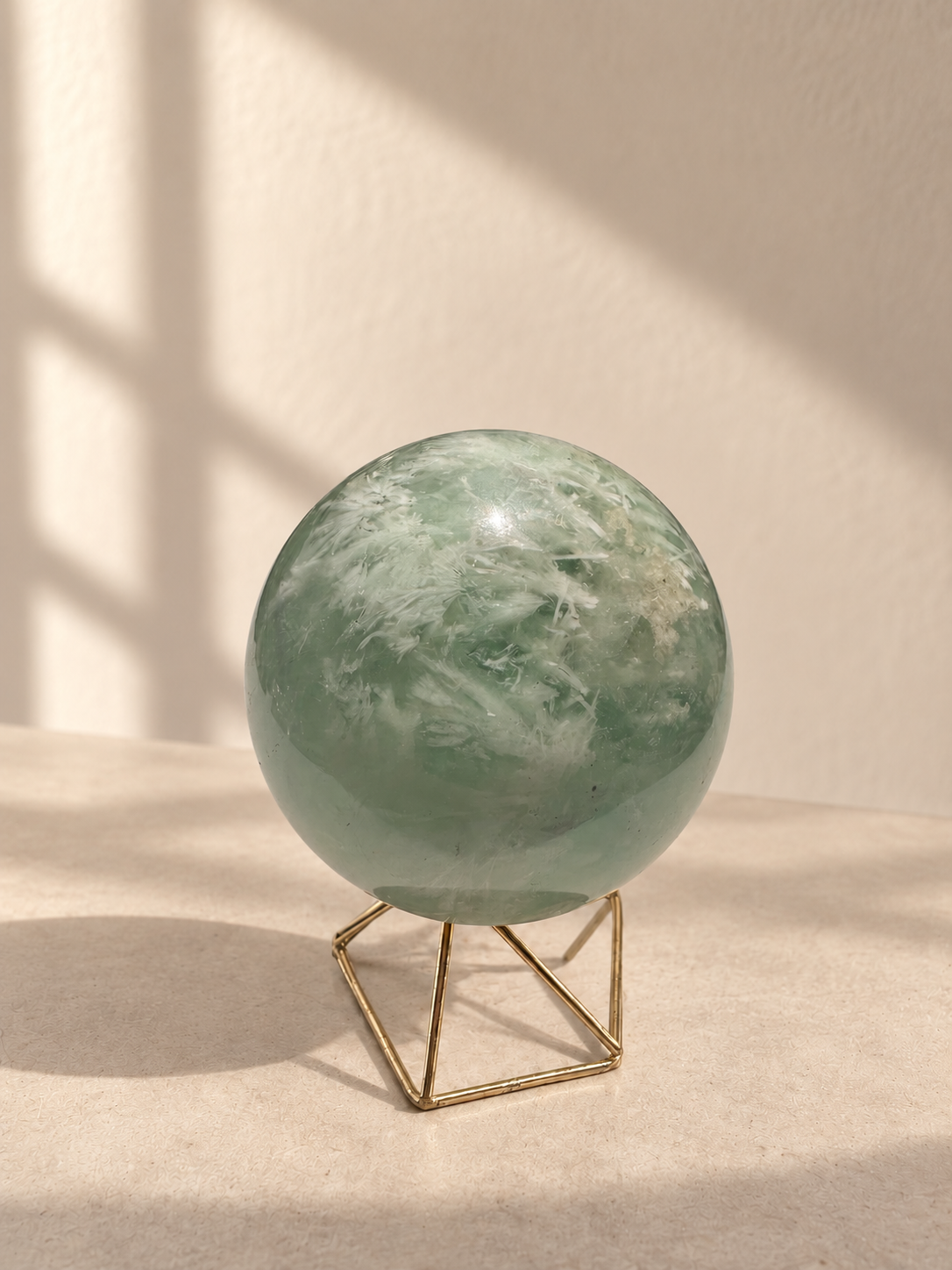 Pale sage green feather fluorite sphere with white plume-like inclusions, alternate view on a metal stand
