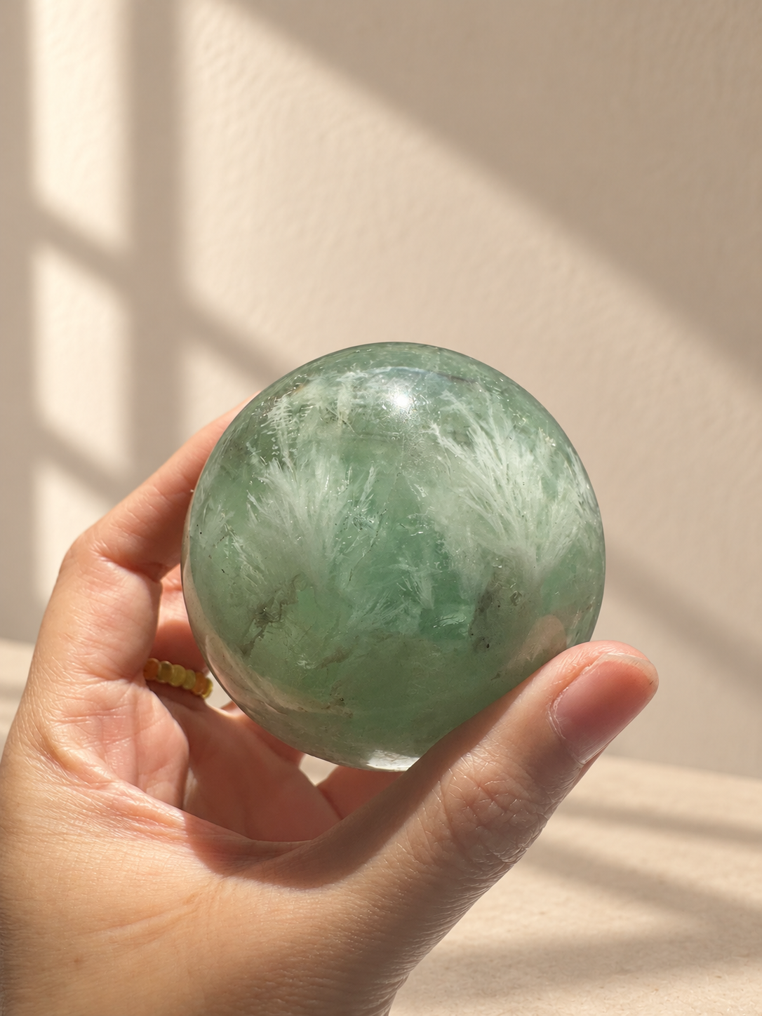 472g feather fluorite sphere held in hand for scale, showing white plumes and dark internal lines