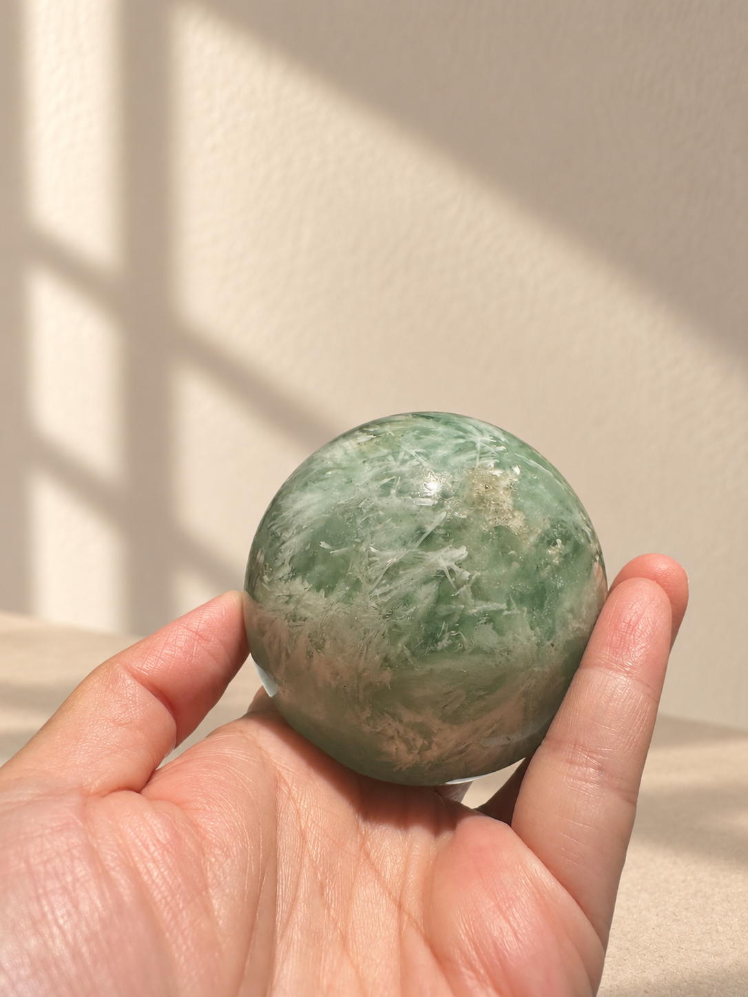 Handheld view of green feather fluorite sphere with dense white plume-like patterns