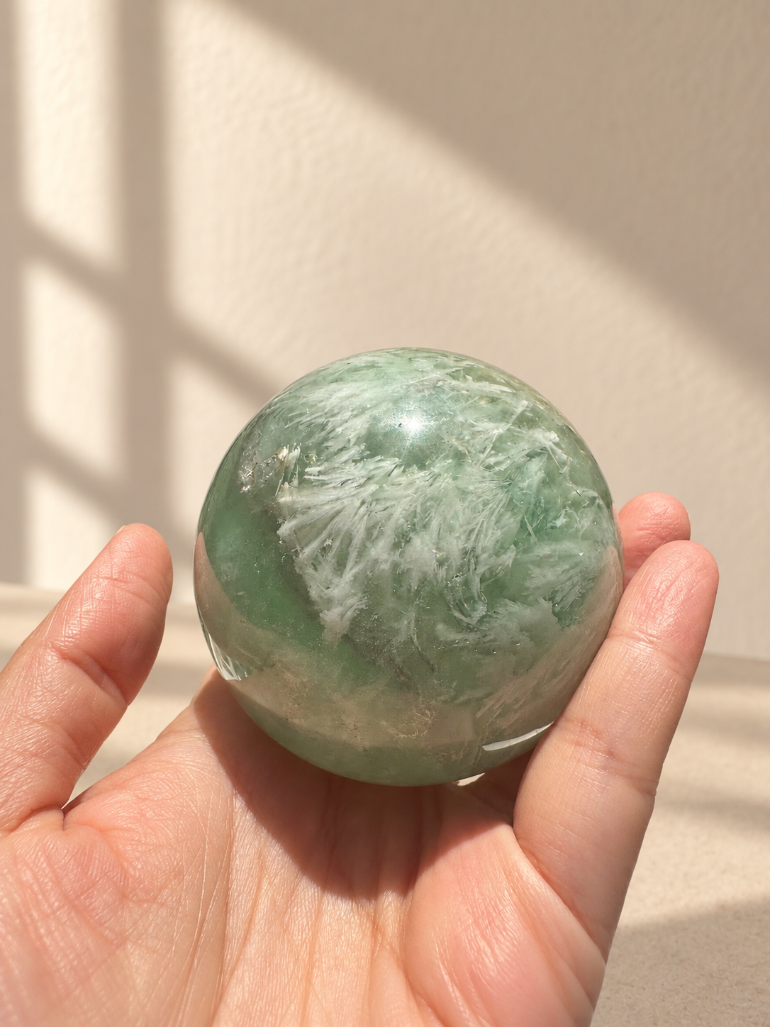 Close handheld angle of feather fluorite sphere showing pale green colour and white inclusions