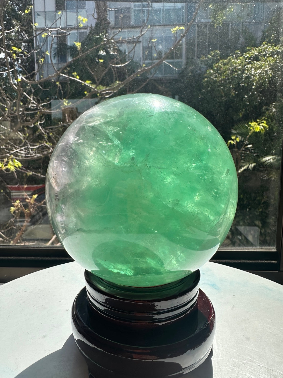 Front view of the large mint-green fluorite crystal ball, with sunlight passing through internal layers and cloudy veils.