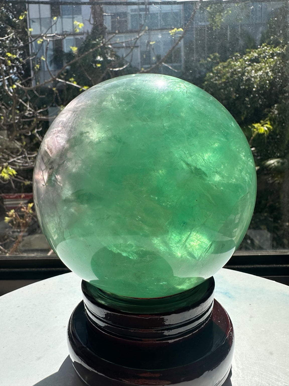 Close view of the mint-green fluorite sphere showing translucent green areas, cloudy white veils and fine internal lines in sunlight.