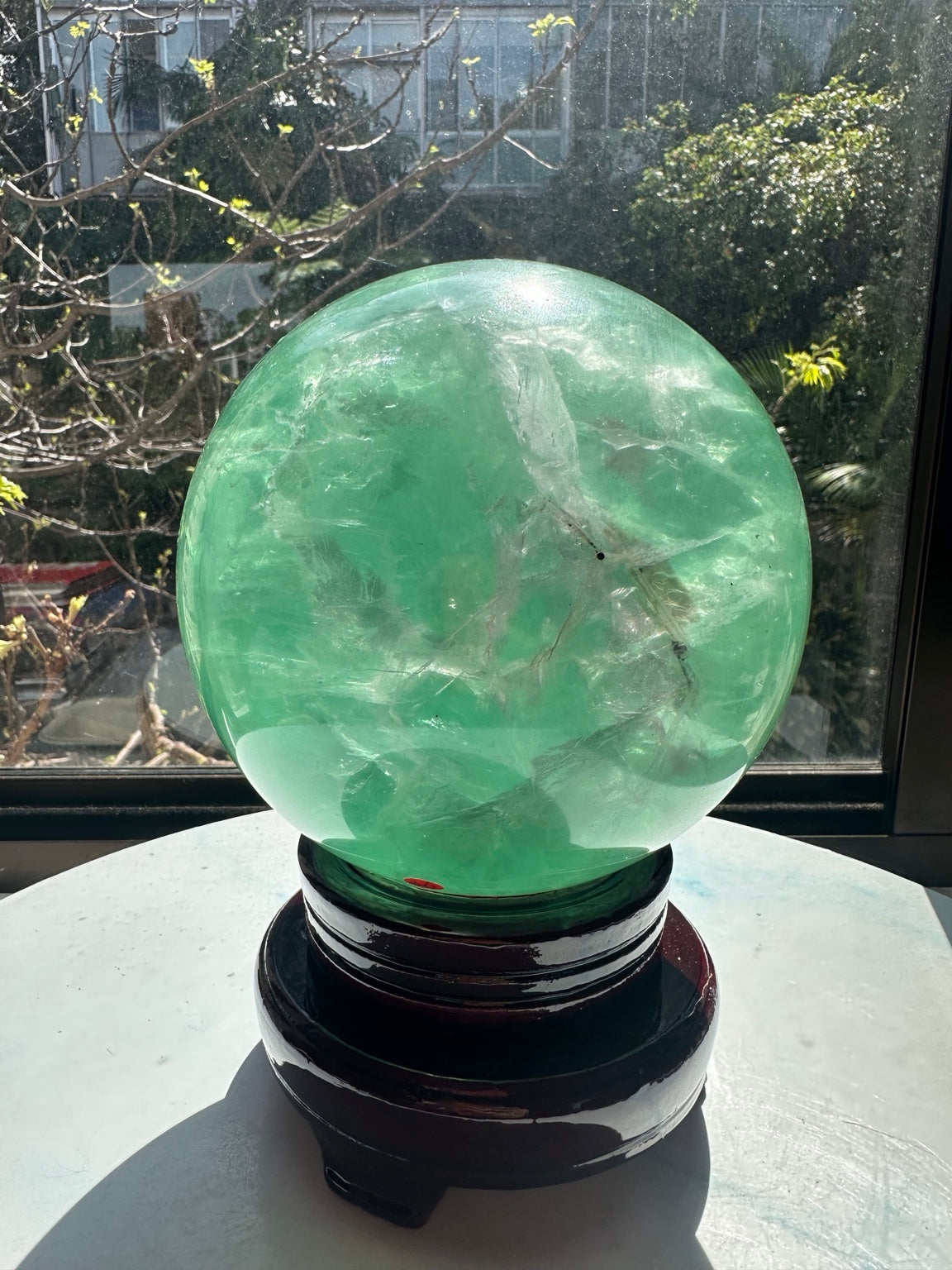 Another side of the large green fluorite ball on its stand, with pale internal veils and several dark inclusions.