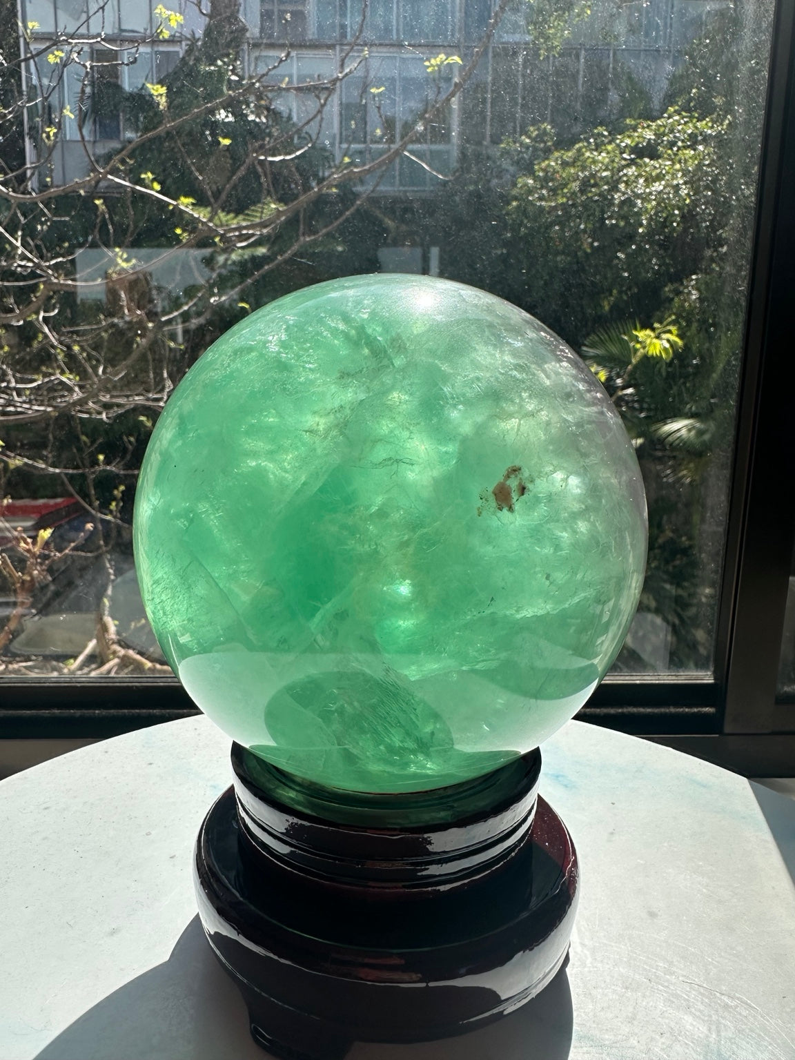Reverse side of the green fluorite sphere showing a brown inclusion and natural internal fracture patterns.