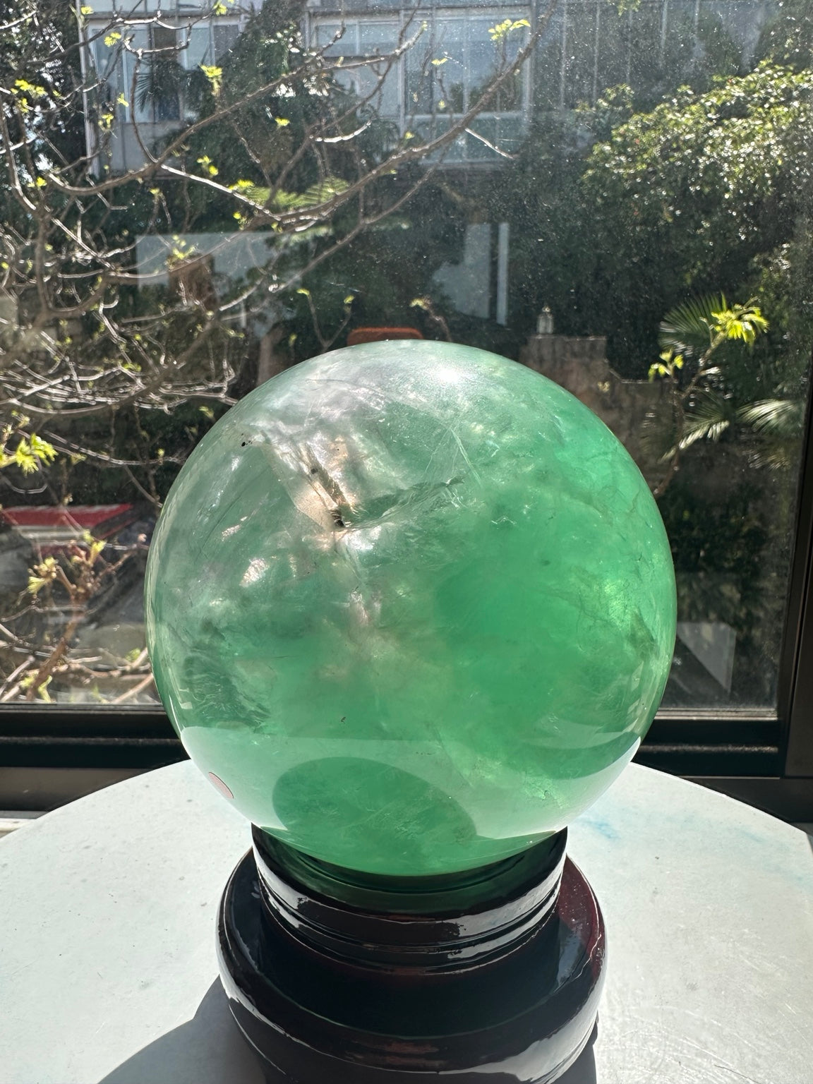 Angled view of the green fluorite ball with clear and cloudy areas and small dark inclusions inside.