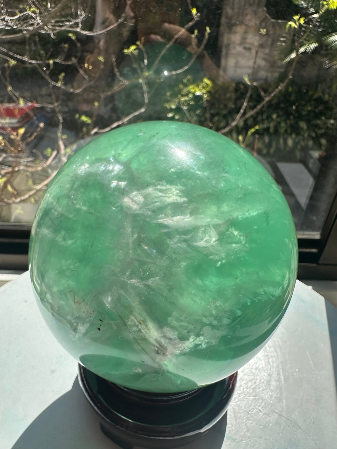 Close-up of the polished green fluorite sphere showing pale veils and dark internal lines in strong natural light.