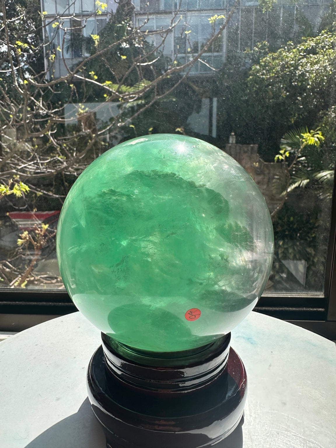Green fluorite sphere from another angle with translucent and cloudy zones and a small inventory sticker.