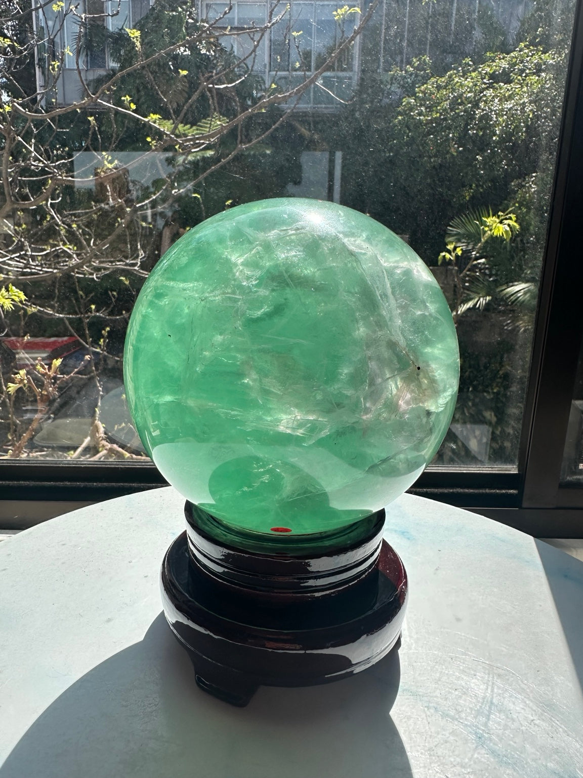 Full view of the 14cm green fluorite sphere and its included dark display stand on a tabletop.