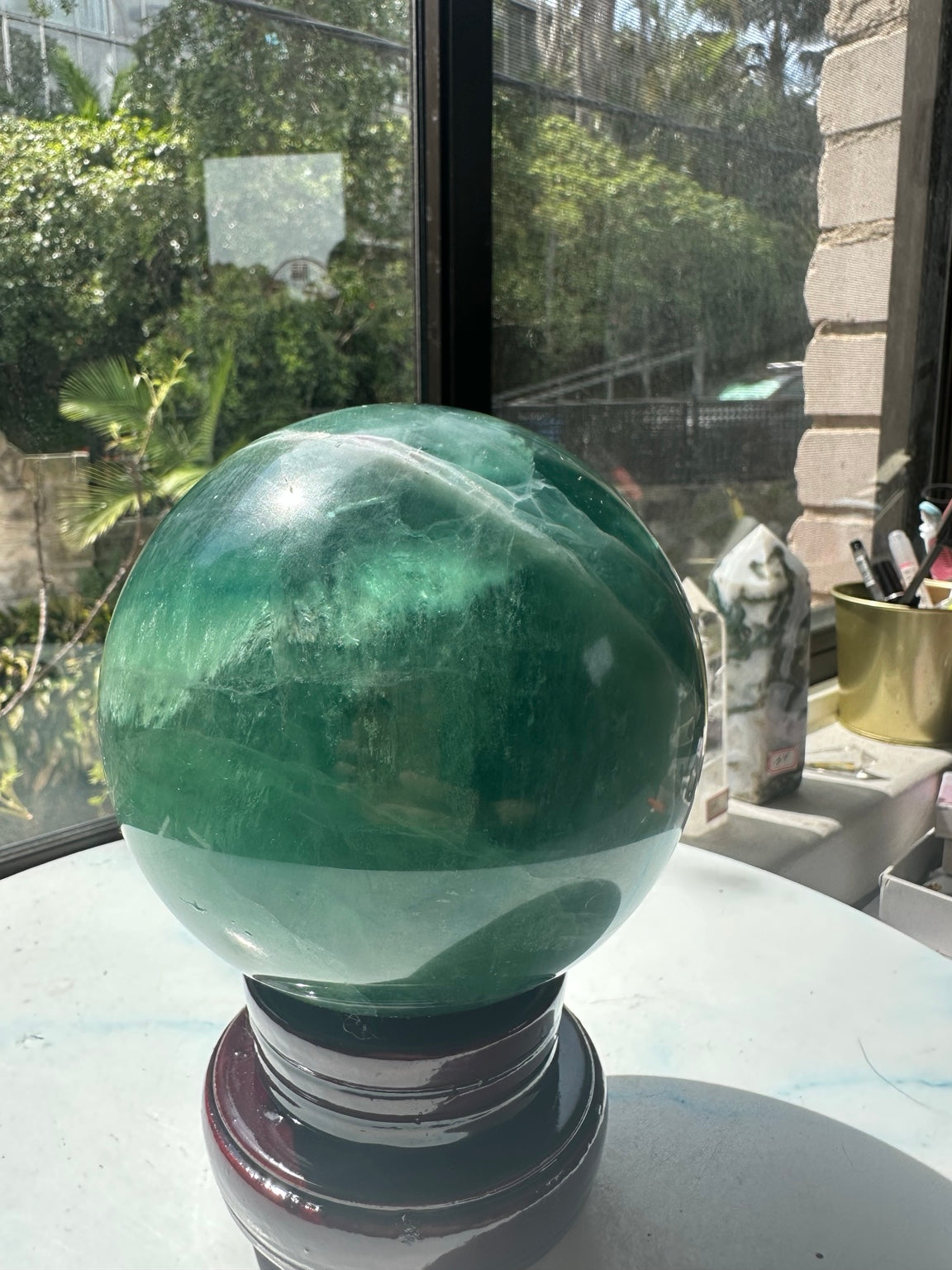 Full 11.5 cm green fluorite sphere displayed on wooden stand near window