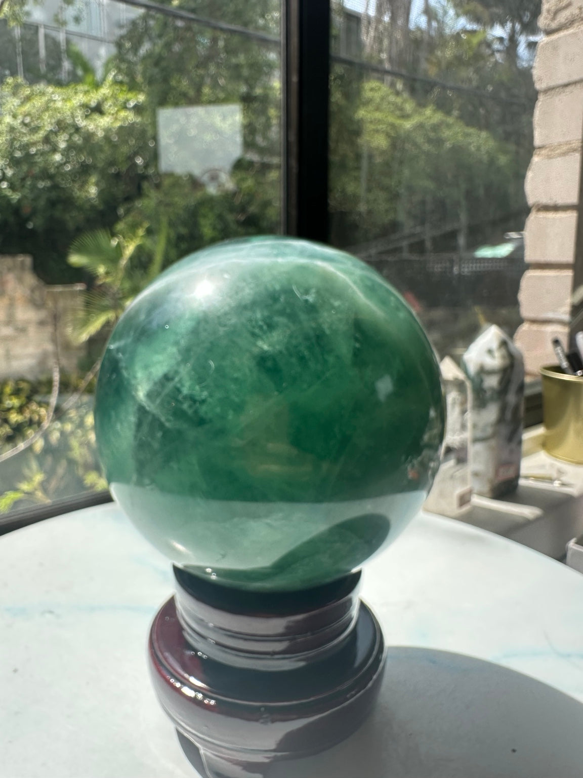 Green fluorite crystal ball photographed in direct sunlight on stand