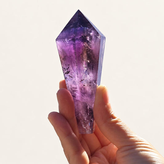 Polished purple amethyst crystal point in soft indoor light.