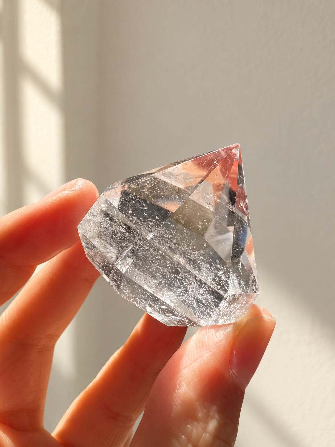 Clear quartz diamond held in a hand, showing polished facets and natural inclusions in soft indoor light.