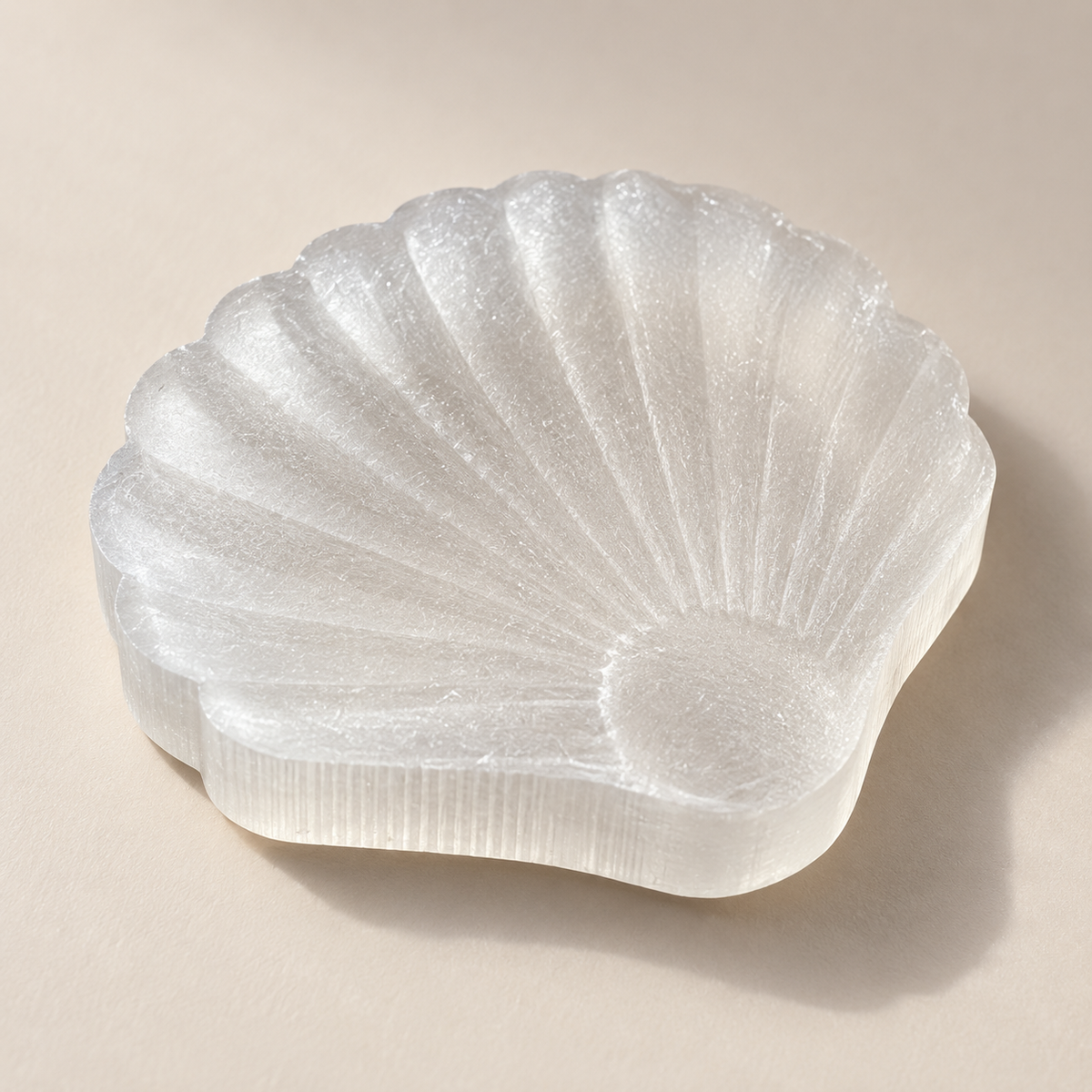 White selenite shell carving with scalloped edges and radiating carved ridges on a warm neutral background, approximately 6–7 cm, sold individually.