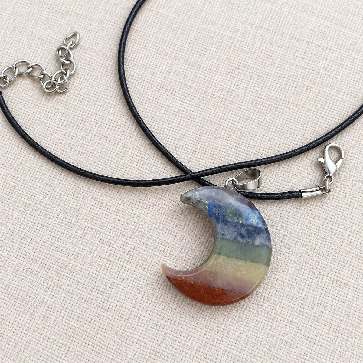 Polished crescent moon chakra pendant showing seven colourful gemstone bands